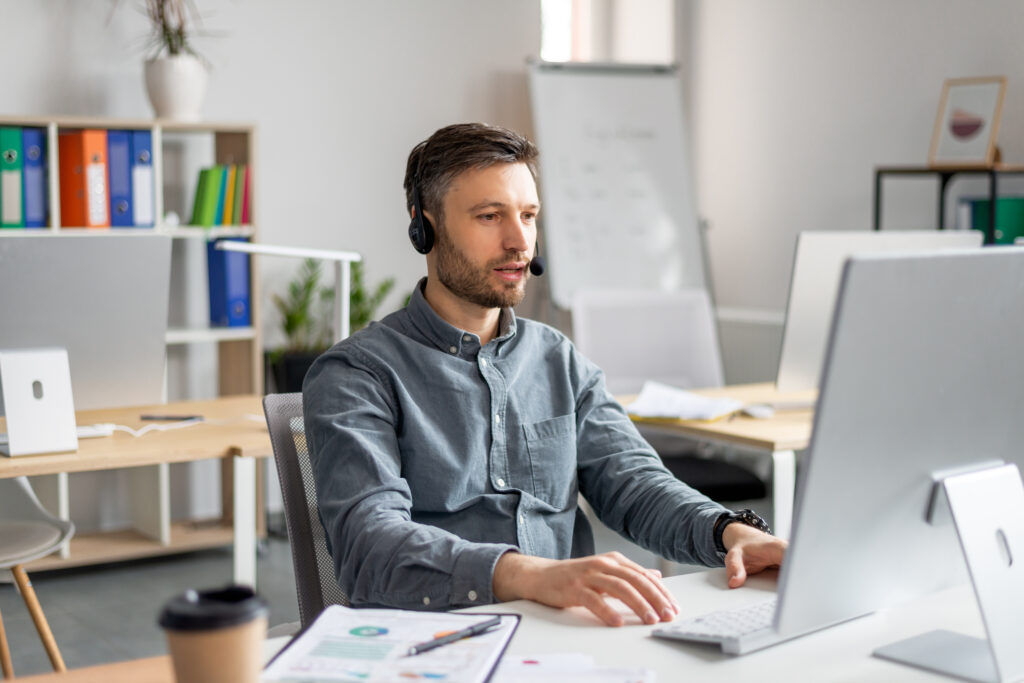 hotline support service. handsome mature male call center operator in headset working on modern computer in office