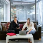 man and woman sitting on couch using macbook