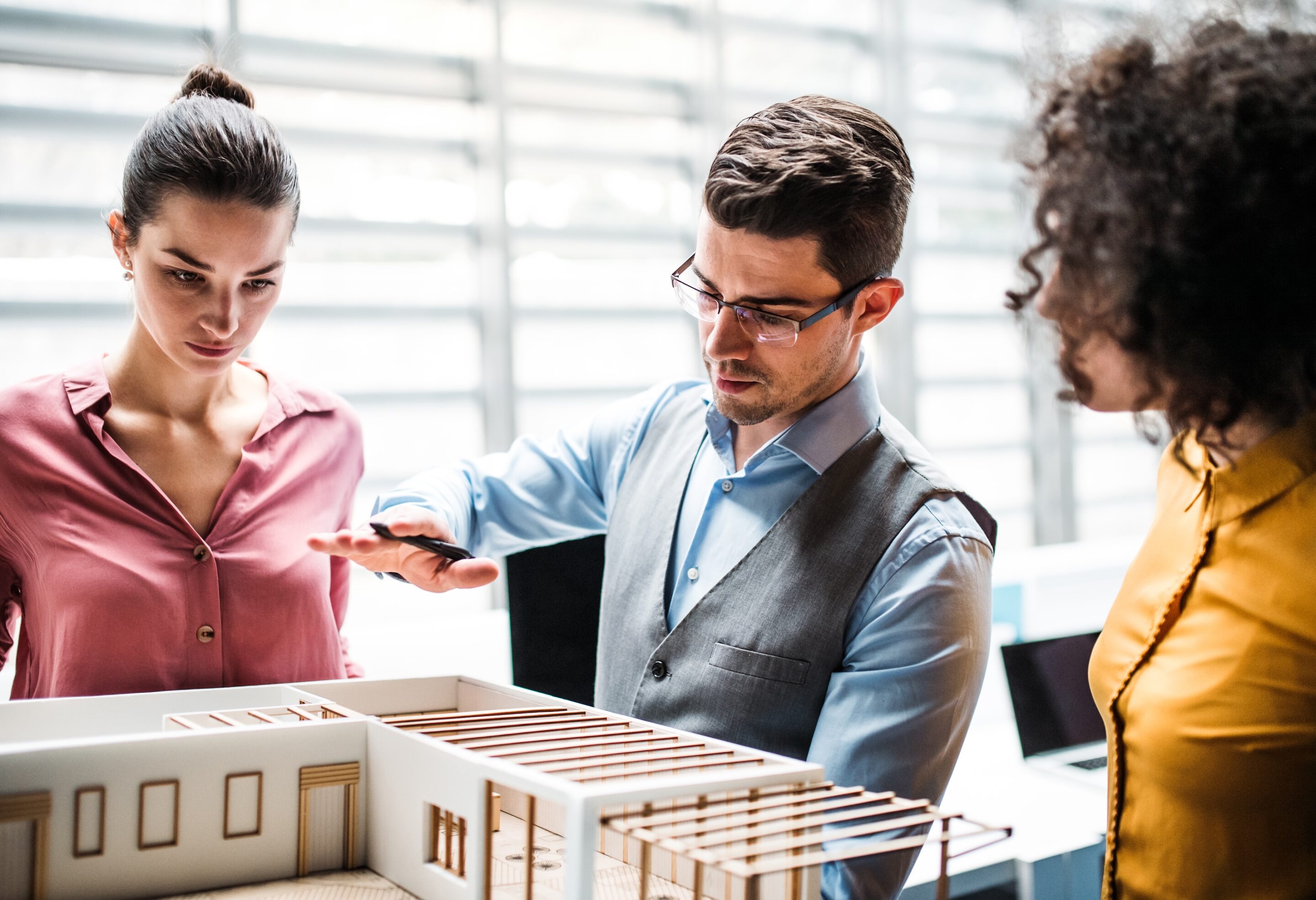 group of young architects with model of a house standing in office, talking.