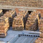 close up stacks of red brick neatly piled on concrete foundation of basement or first floor of future house for walls construction on sunny summer day. building, investment, delivery concept.