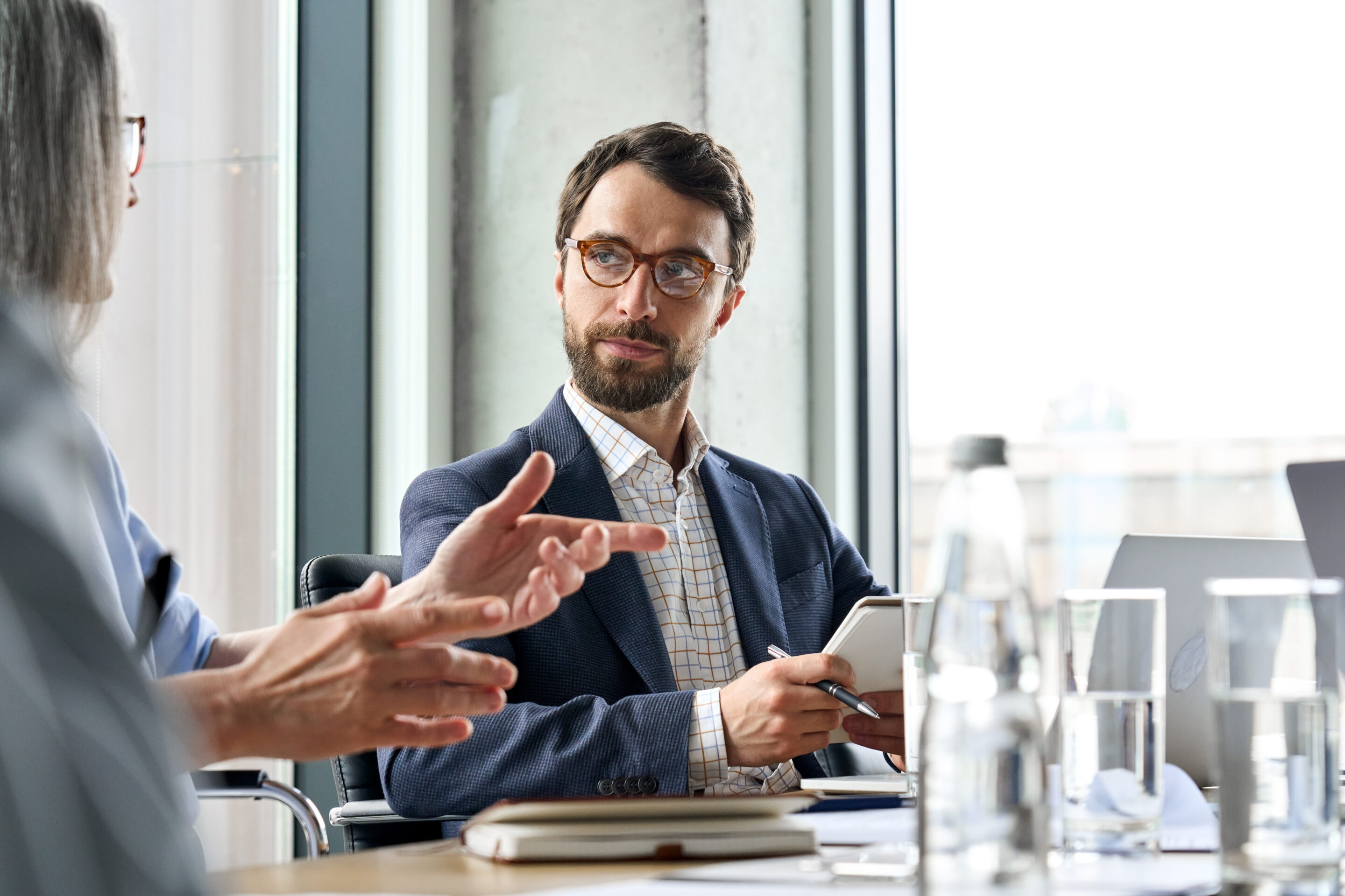 serious male ceo listen to female colleague holding notebook at table meeting.