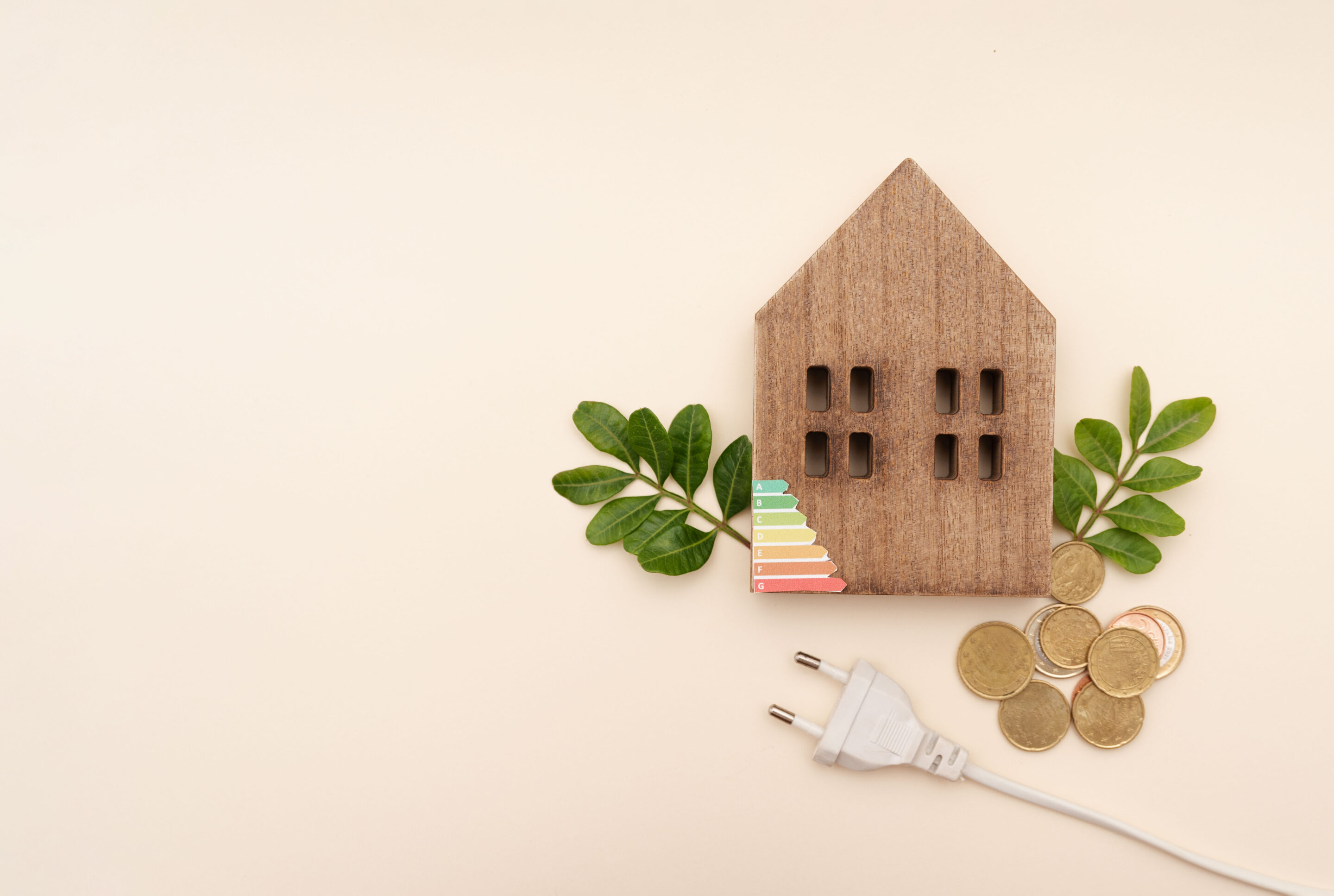 wooden house model with green leaves and coins and power plug on neutral background,sustainable energy and electricity home prices concept