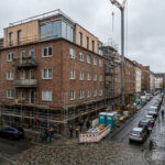 Moderne Dachaufstockung auf einem älteren Wohngebäude in einer dicht bebauten deutschen Innenstadt mit sichtbarer Baustelle, Gerüst und beobachtenden Bewohnern auf Balkonen. Diese Bild wurde mithilfe von KI erstellt.