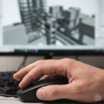 Detailaufnahme einer Hand auf Maus und Tastatur in aktiver Bewegung. Bildschirm im Hintergrund unscharf mit abstrakten 3D-Strukturen in Archicad.